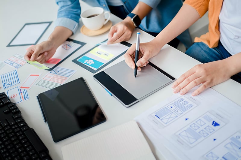 a group of people sitting at a table with a tablet, pen and paper